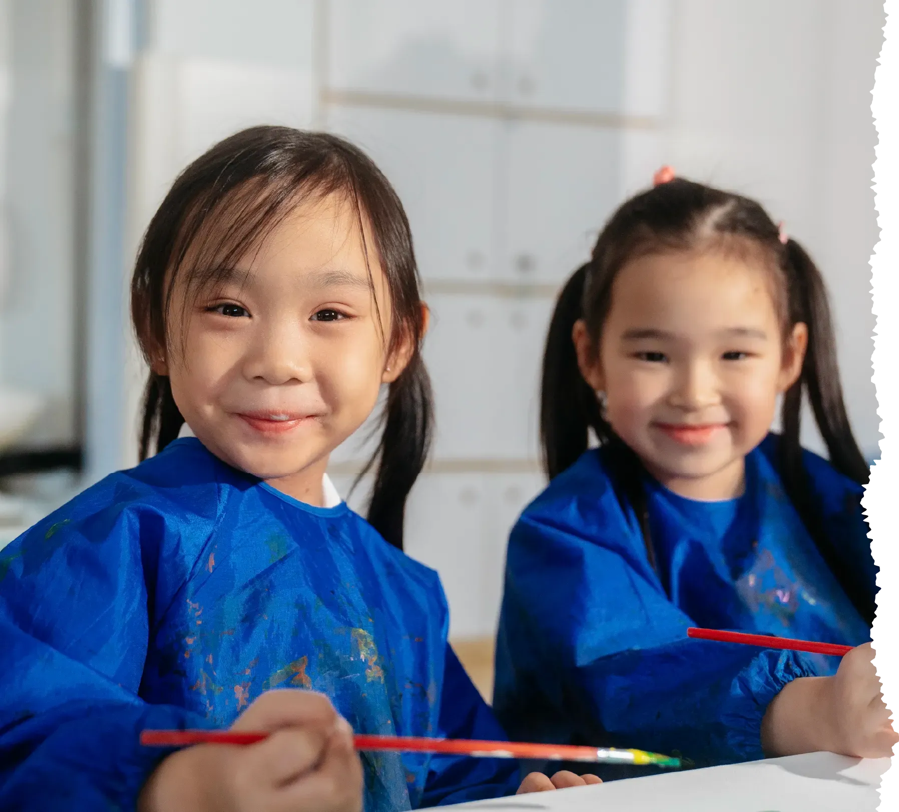 Two smiling Posso Preschool girls in art smocks