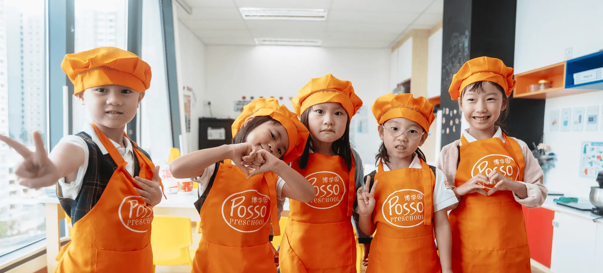 Posso children in orange chef hats and aprons making heart shapes with their hands