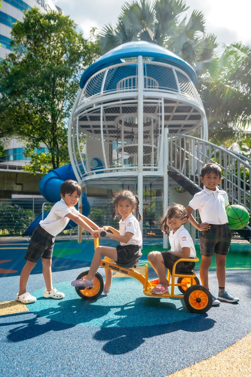 Children with a tricycle under the rocket tower on the outdoor playground at Posso Jurong East