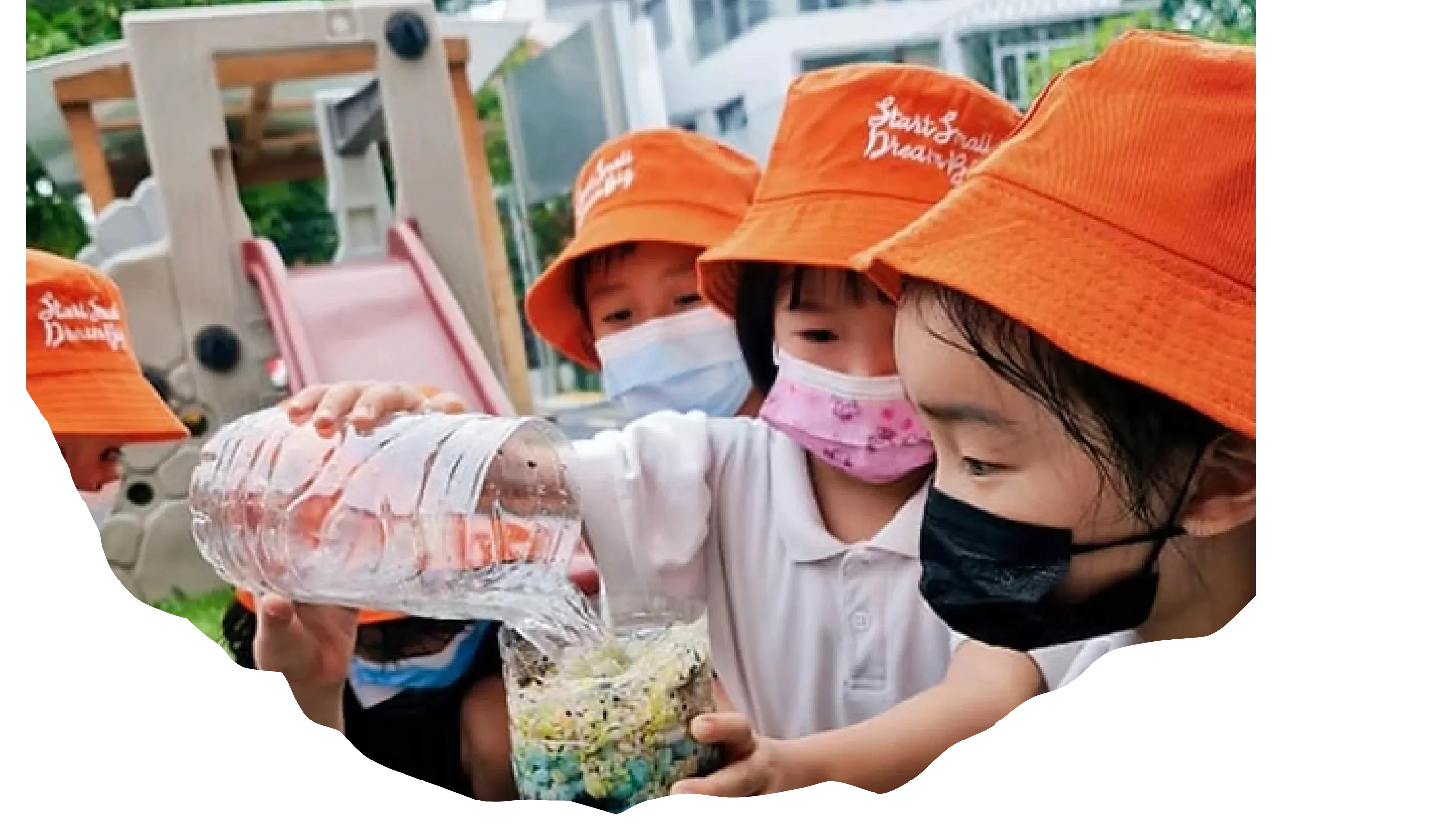Two Posso children in orange hats doing a sensory activity with a bottle