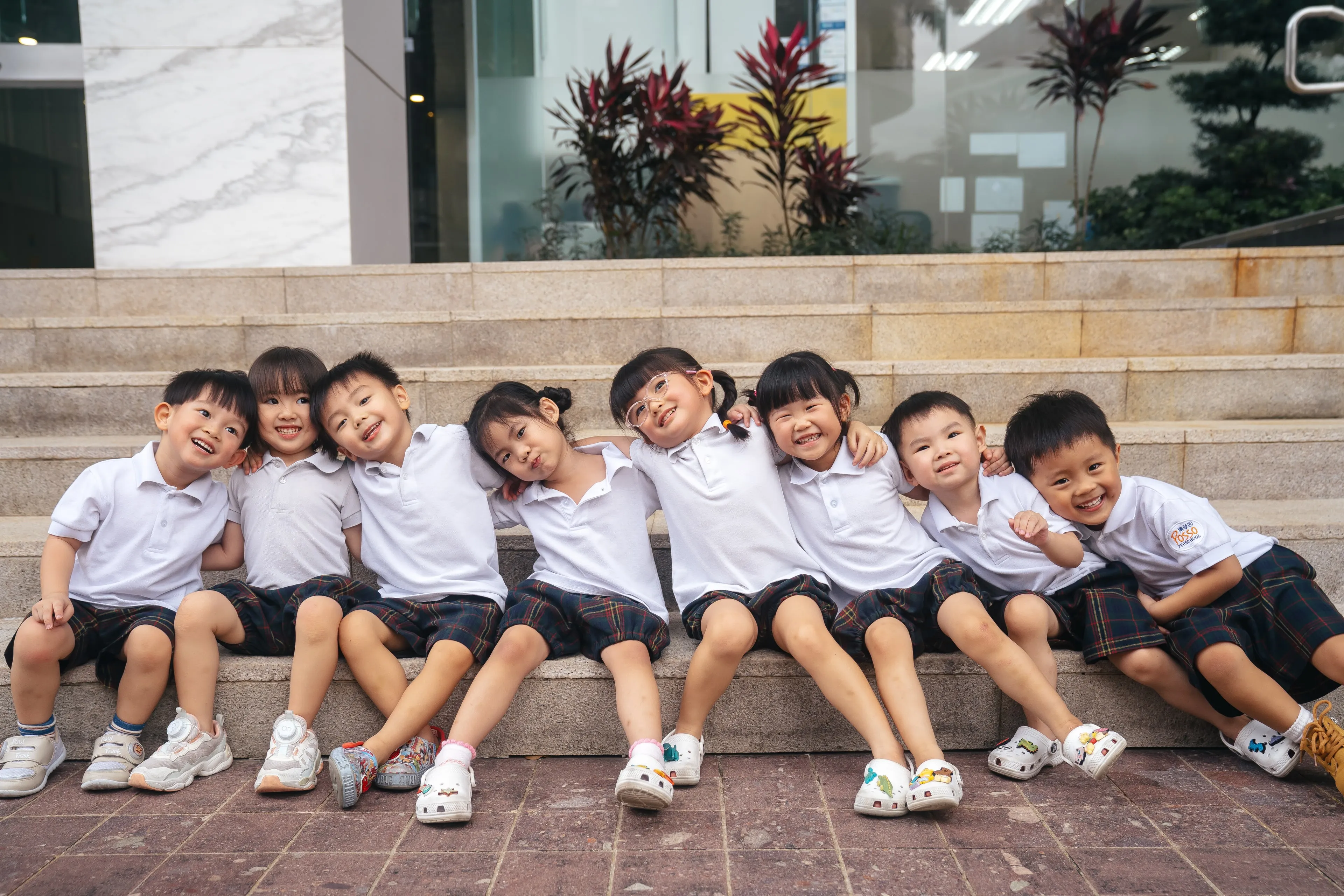 Posso Preschool children in uniform sitting together on steps, arms around each other and smiling